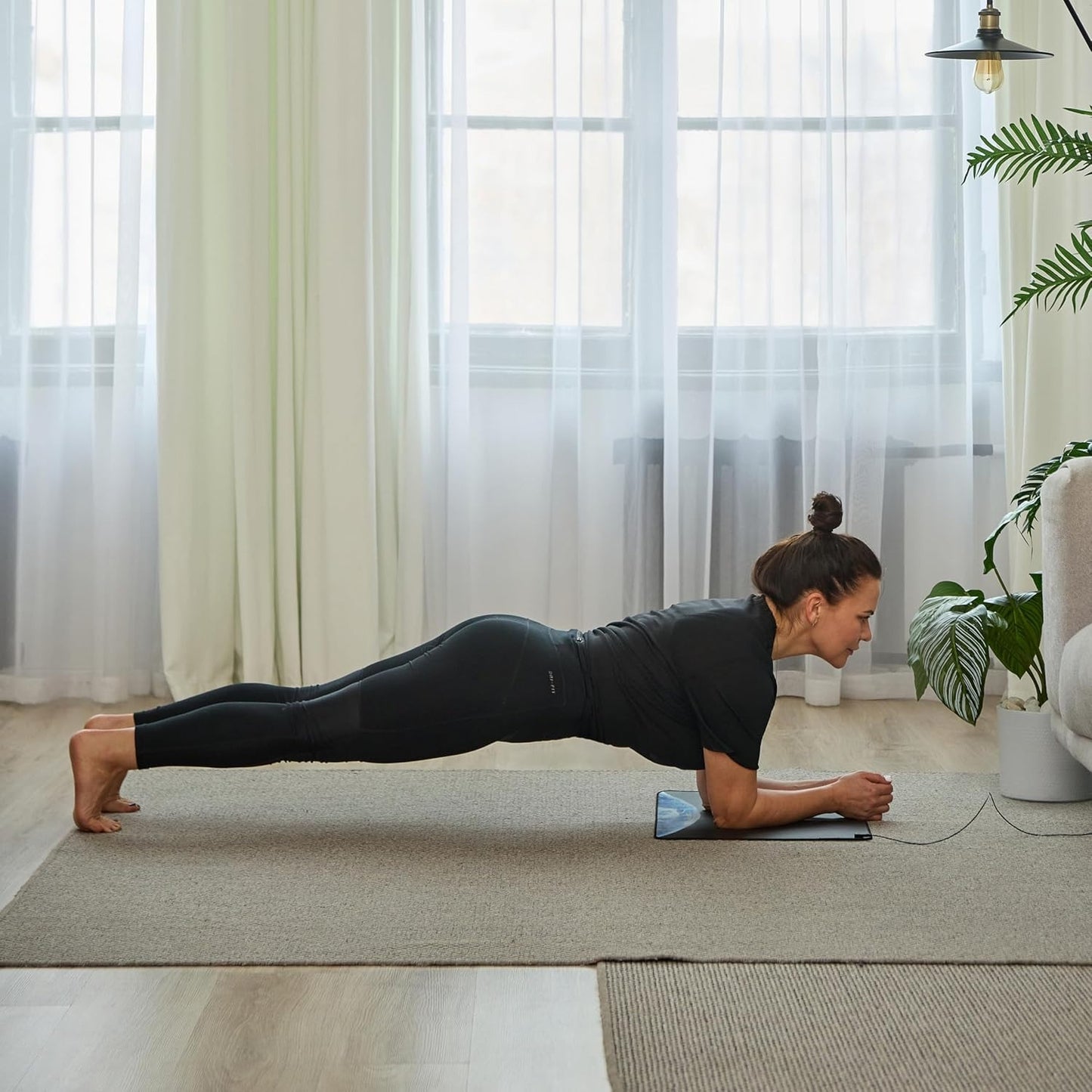 Woman performing a plank exercise in a home setting on Rejuviaa mat with large windows and plants.